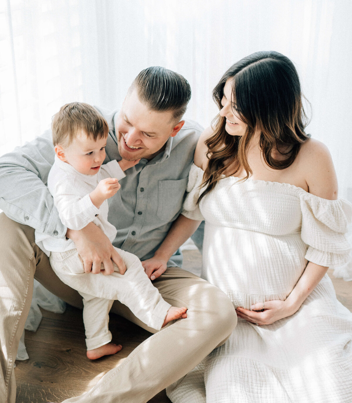 maternity mother holding her belly sitting next to her husband and son