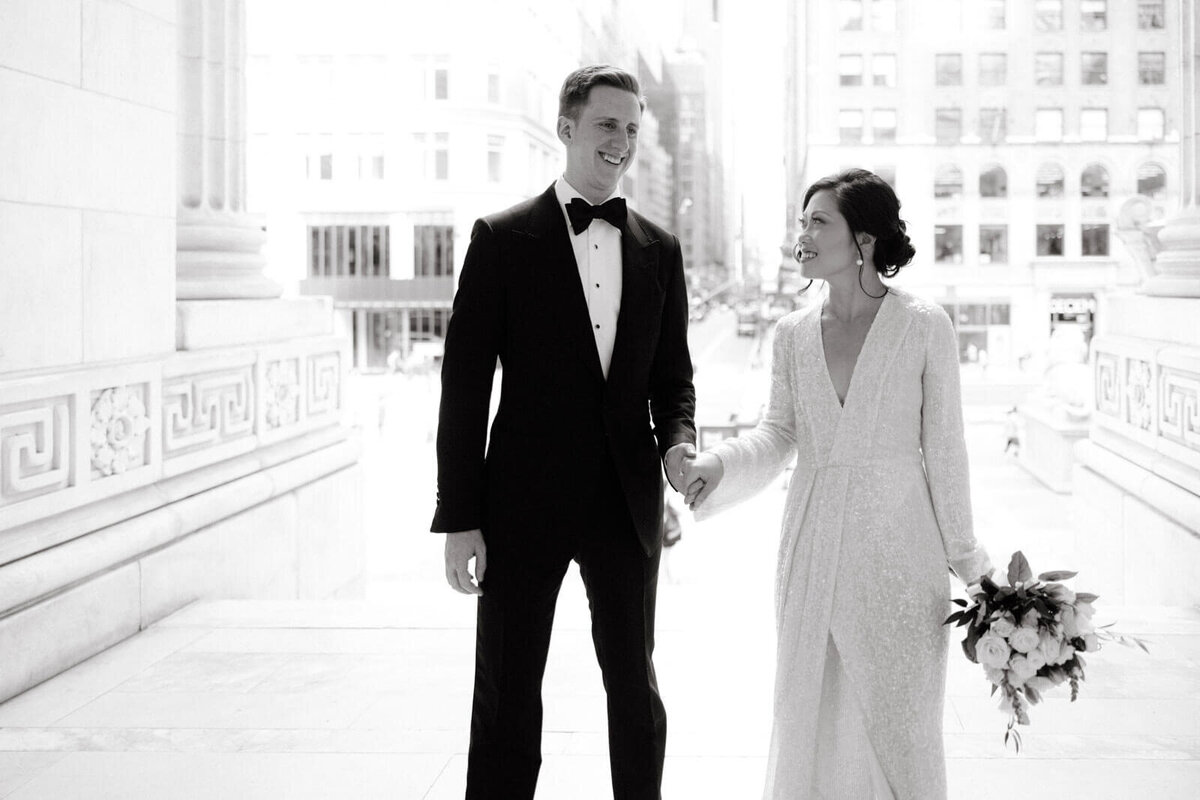 The bride and the groom are happily entering the New York Public Library, buildings in the background. Image by Jenny Fu Studio