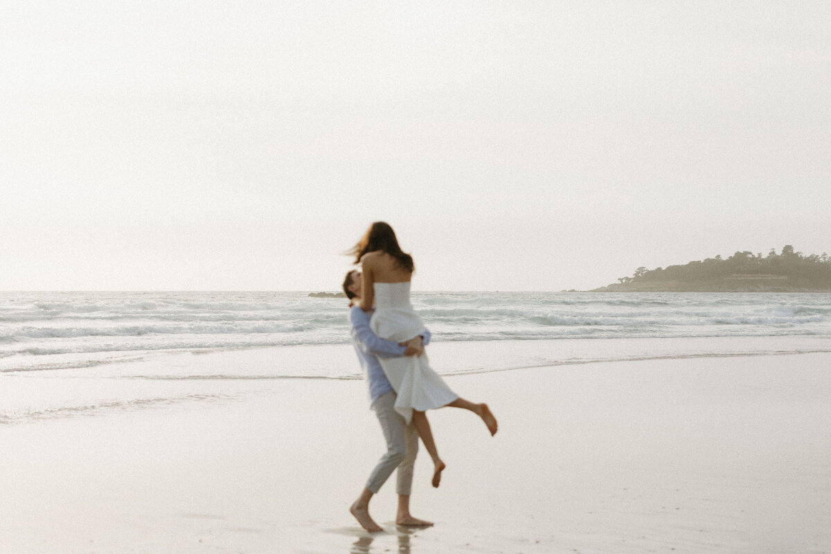 Couple in dress clothes dancing around on California coast along the shoreline