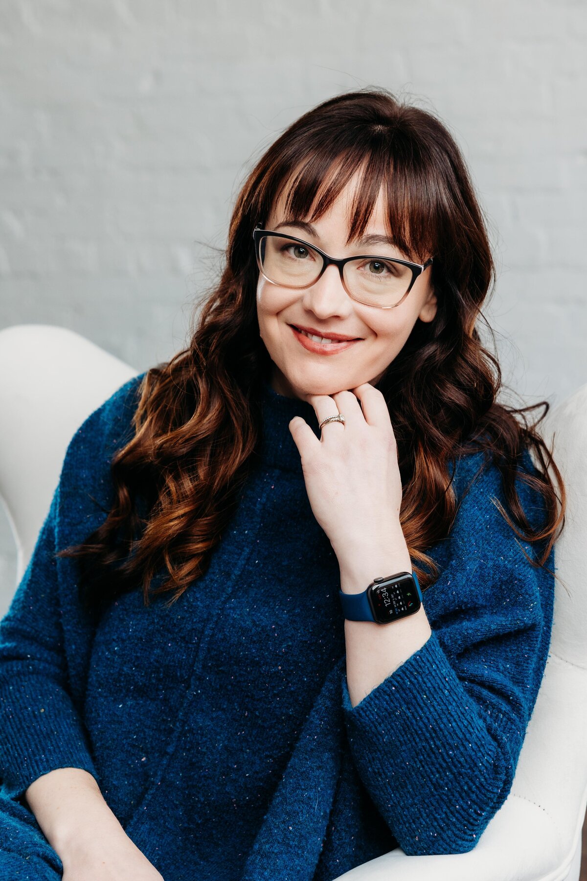 Woman sitting in a white chair posed for a headshot.