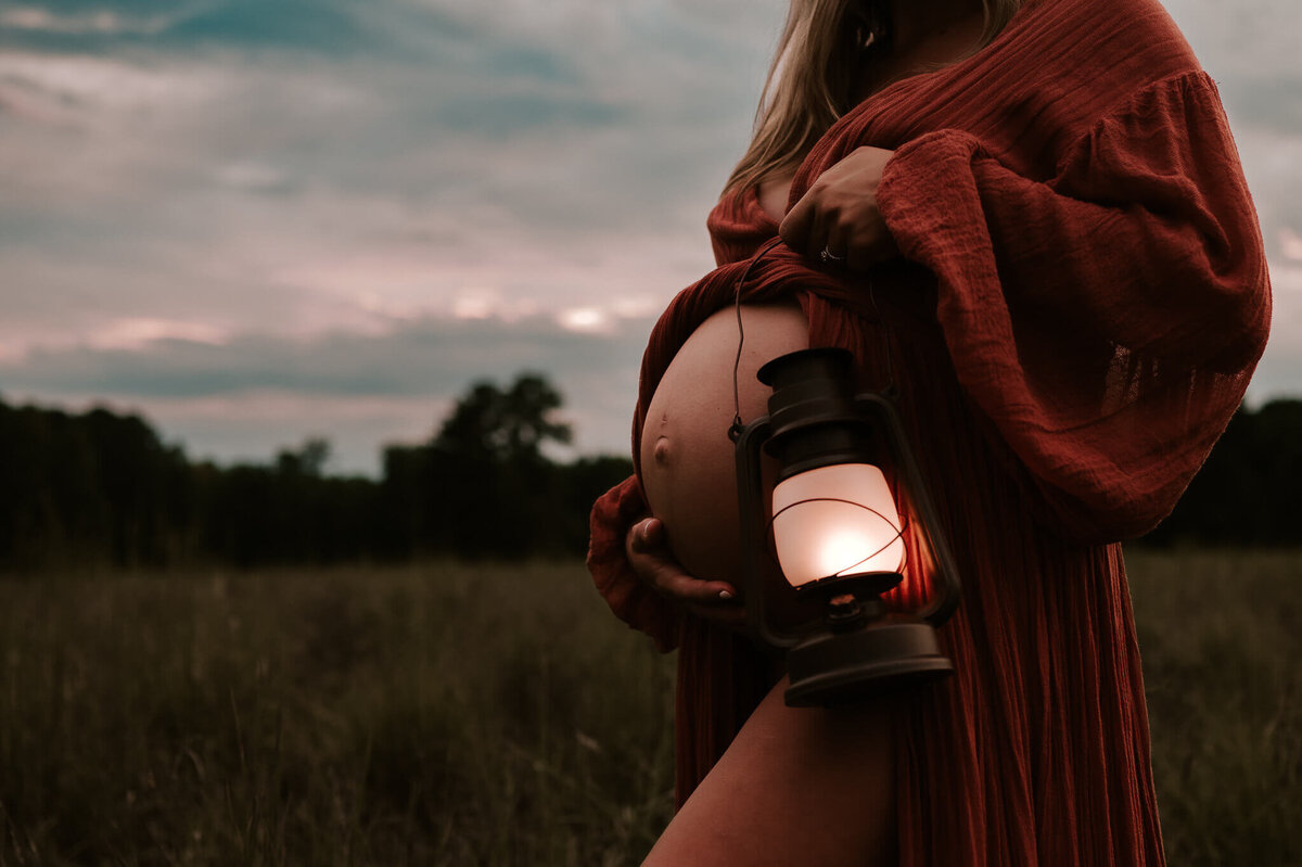 Mom touching her pregnant belly while holding a lantern during a sunset maternity session in charlotte