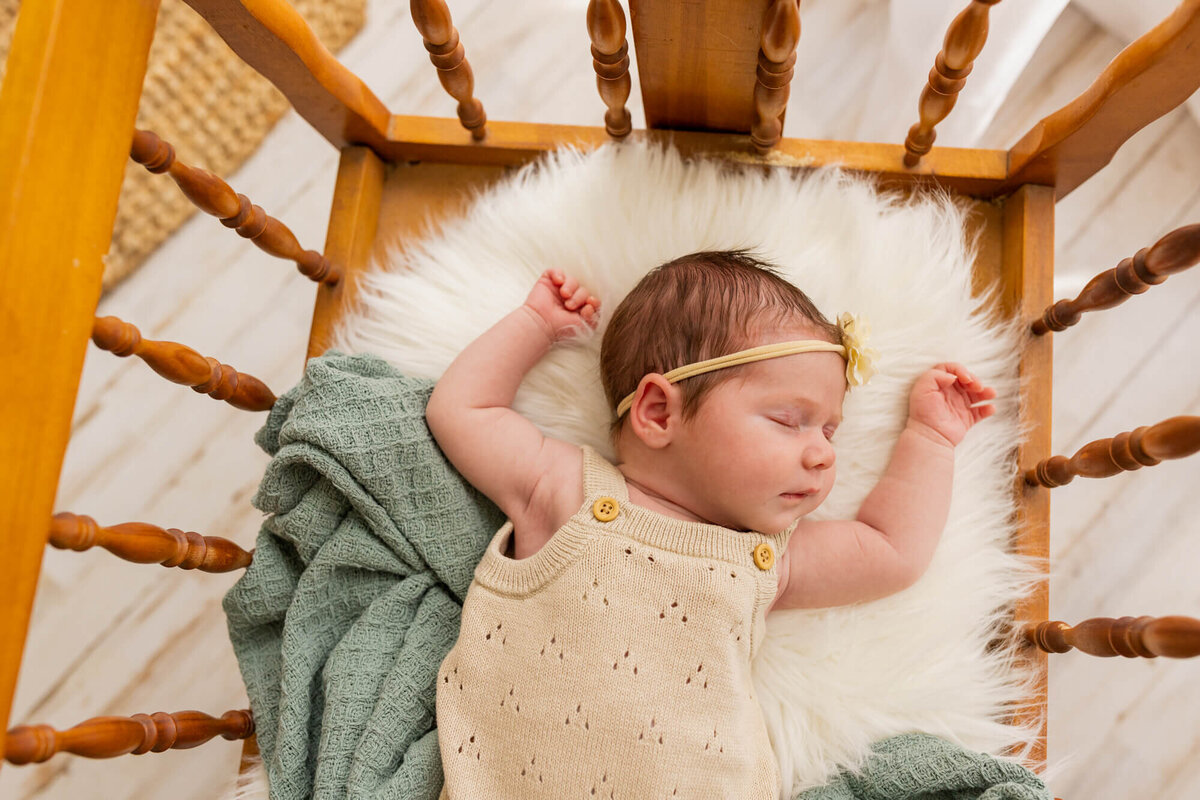 Newborn baby girl in a cream bubble and bowlaying  on a furry blanket in an antique wooden crib