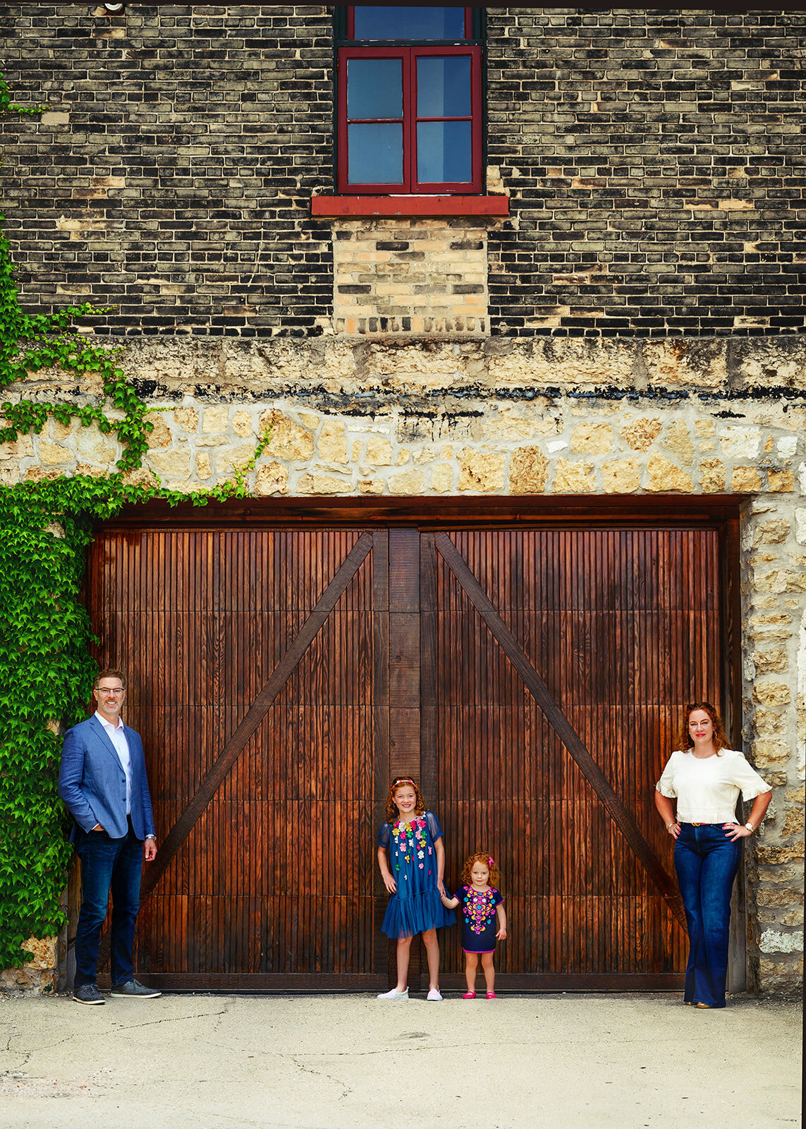 family posed against a brick building with rustic barn door with climbing vines