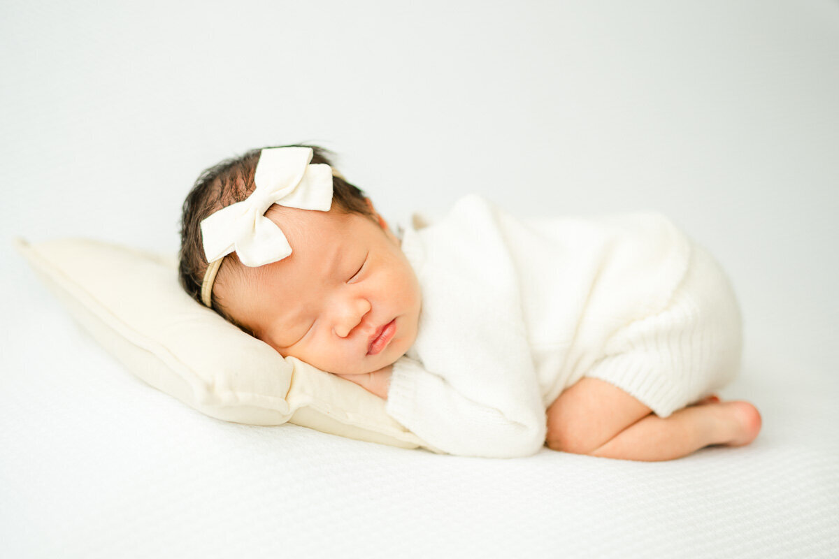 an infant girl lays on her stomach with her head resting on a pillow while captured by an Austin newborn photographer.
