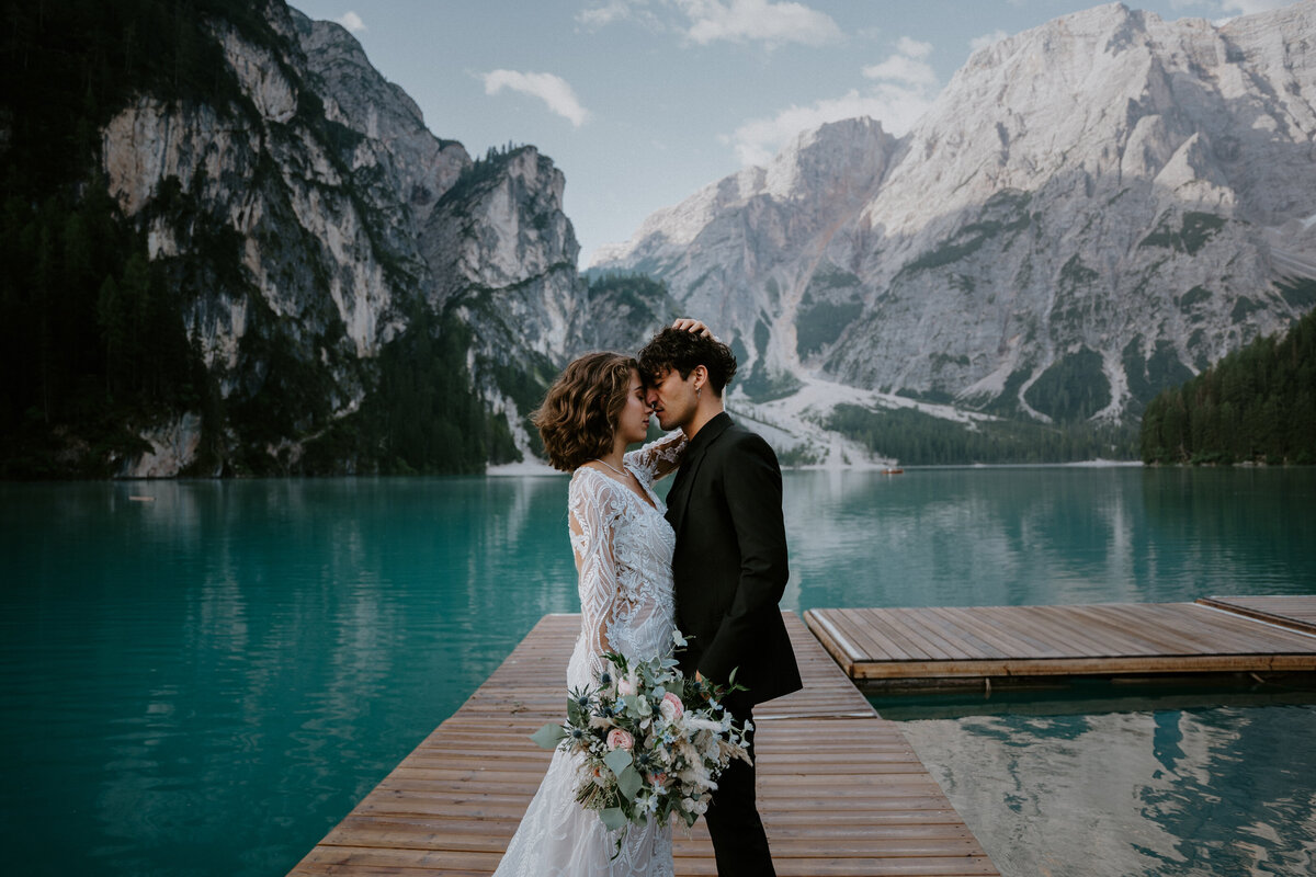 lago di braies italy elopement photographer, couple stands on boat launch over the blue lake with mountain background
