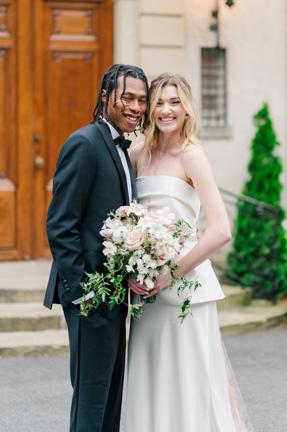A bride smiling widely and her groom smiling with her outside of Glen Manor House. 