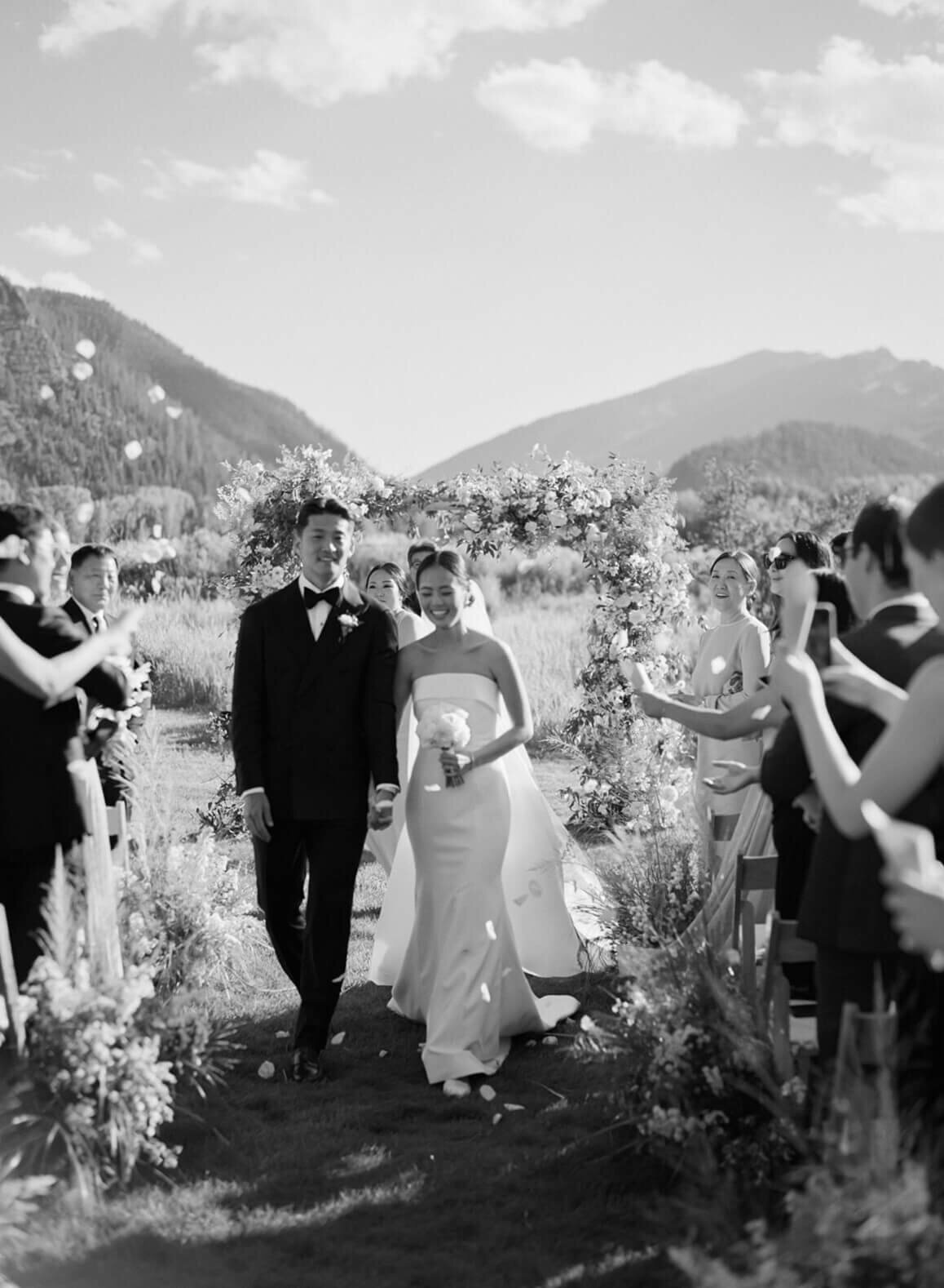 Bride and groom walking down the aisle during their ceremony recessional at Aspen Meadows Resort, surrounded by guests and nature.