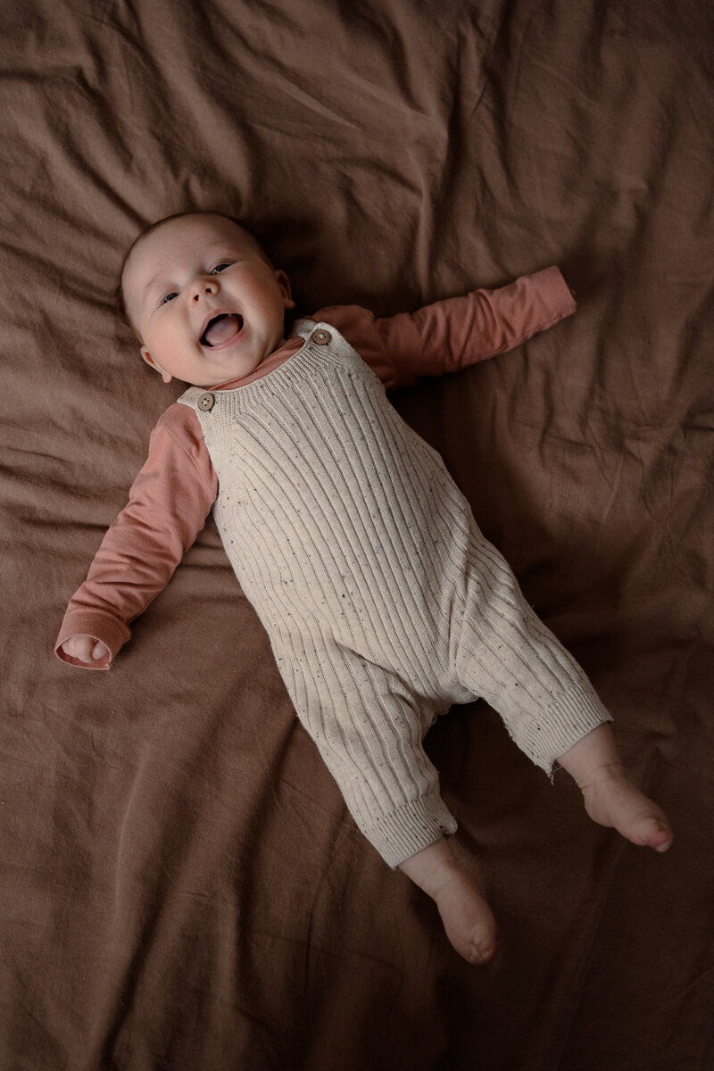Lachende baby liggend op bed tijdens een newbornshoot