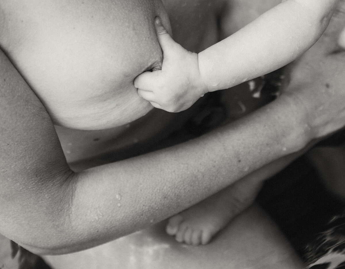 Closeup shot of a child’s hand holding onto mother’s breast. Tender family photography capturing intimate moments in Portland and Nashville.