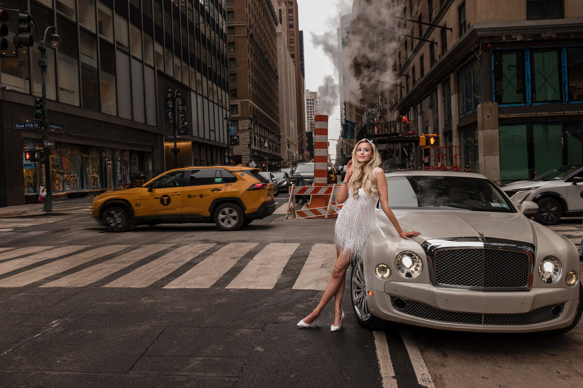 Bride in a beaded mini dress leans against a white Bentley at the corner of Lexington Avenue and East 47th Street, surrounded by NYC steam stacks, construction, and a yellow cab in motion—an editorial-style portrait blending high fashion and classic New York wedding energy.