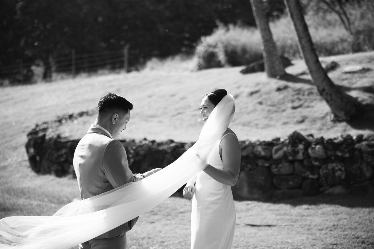 Black and white photo of the bride’s veil blowing in the wind, with the bride and groom captured in a documentary wedding photography style — Carmel wedding photography by Kate Winters Photography.