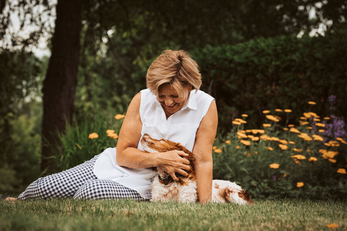 woman sits on grass and hugs small dog