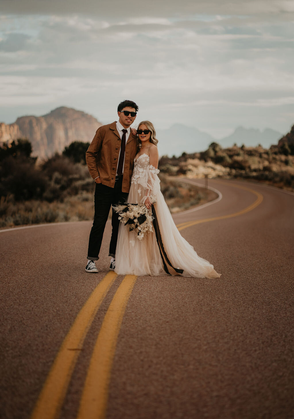 Bride and groom standing in road with sunglasses