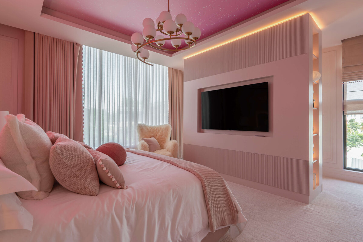 Pink girl's room with a television recessed into the wall across from the bed. Above there is a contemporary chandelier.