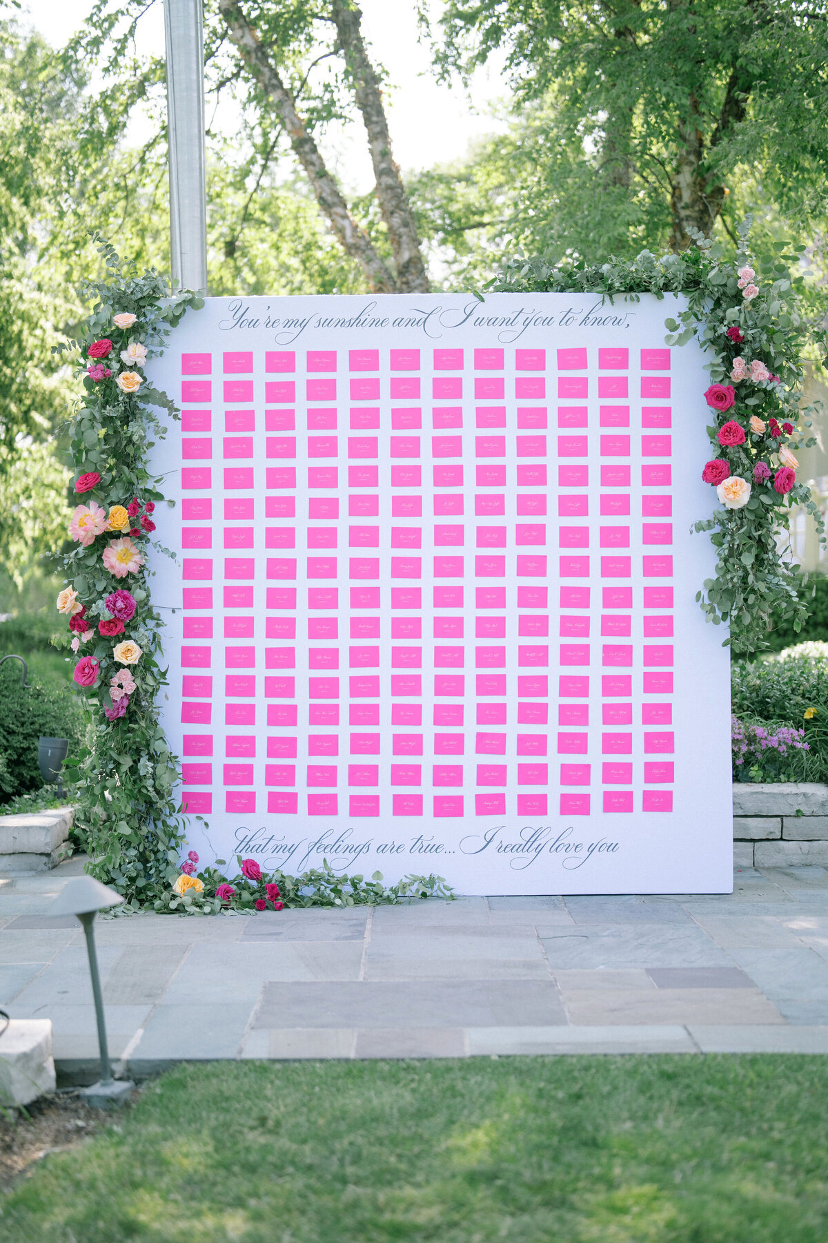 A floral photo wall with pink seating chart, inviting guests at Saddle Country Club.