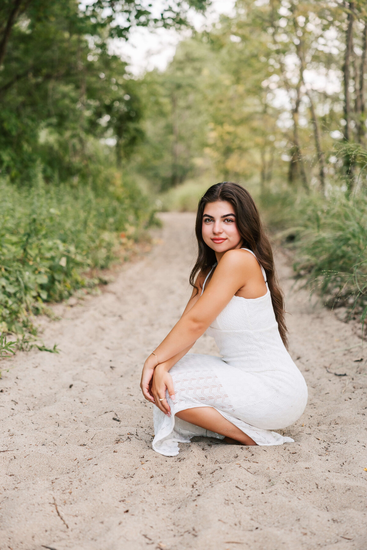 Photo of a senior girl stooping down in the sand in Erie Pa