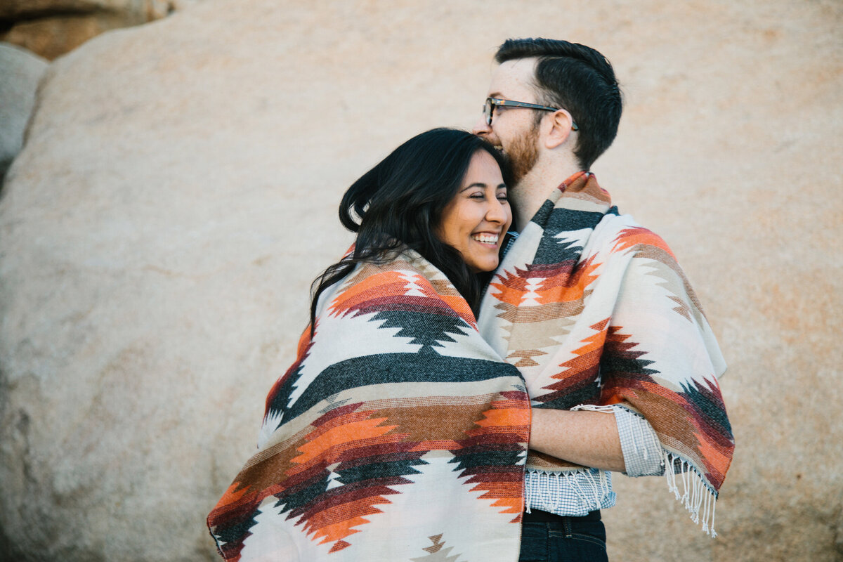 man and woman laugh and embrace in blanket
