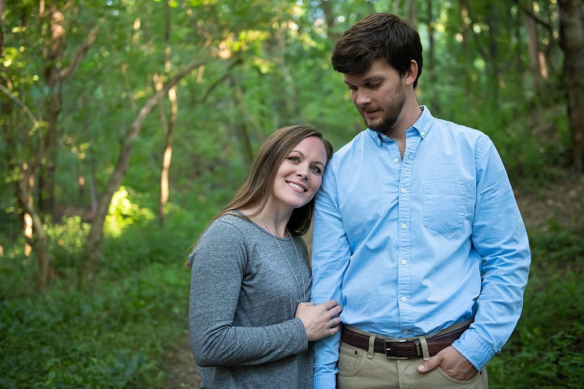 Bride-to-be rests head on fiancé's shoulder during engagement session on a wooded trail in Pittsburgh, PA