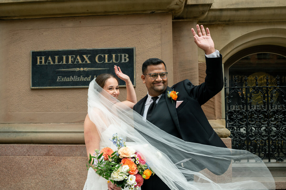 Wedding couple wave to cars as they stand outside Halifax Club