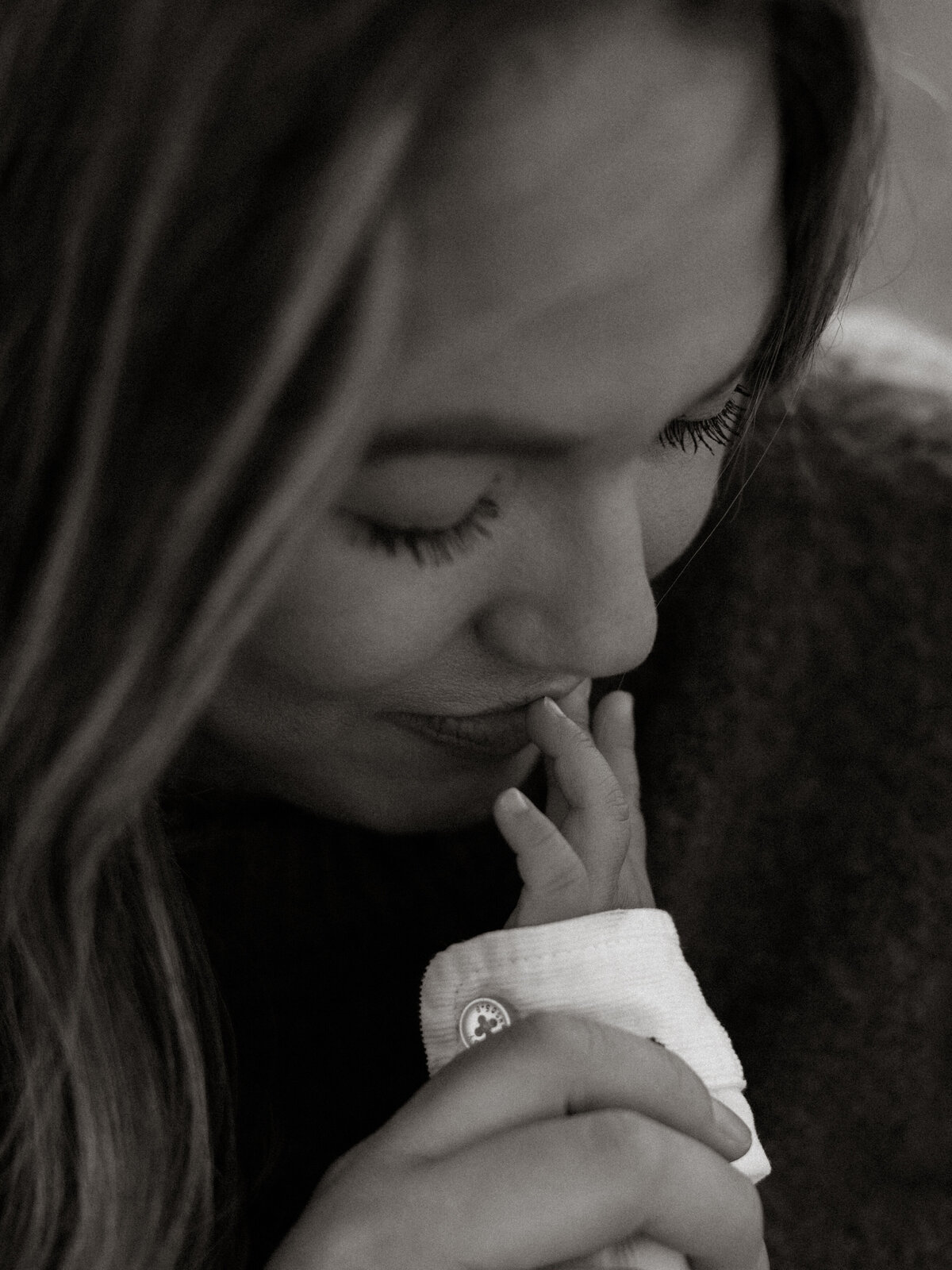 Close-up of a mother kissing her newborn’s tiny fingers, captured in black and white to preserve the emotional stillness of the moment.