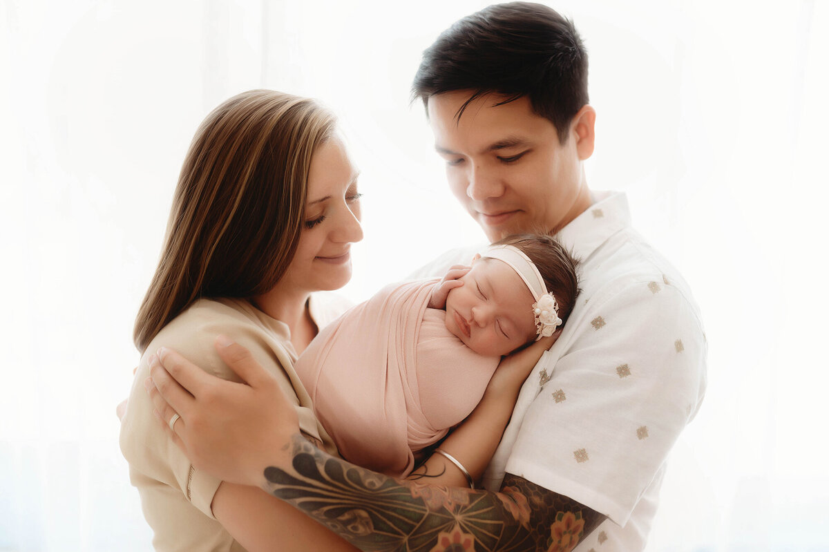 Parents embrace their infant daughter during Newborn Portrait Session in Charleston, SC Newborn Photography Studio.