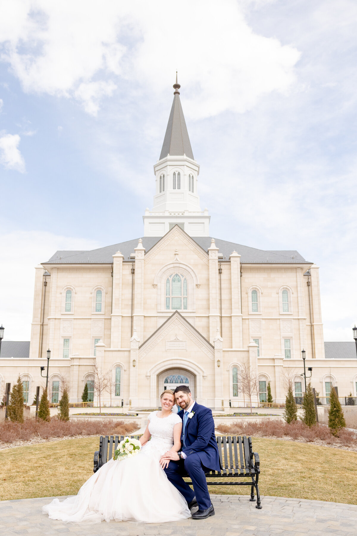 Bride and groom sitting on a bench in front of the Taylorsville Utah Temple, smiling and enjoying a peaceful moment.