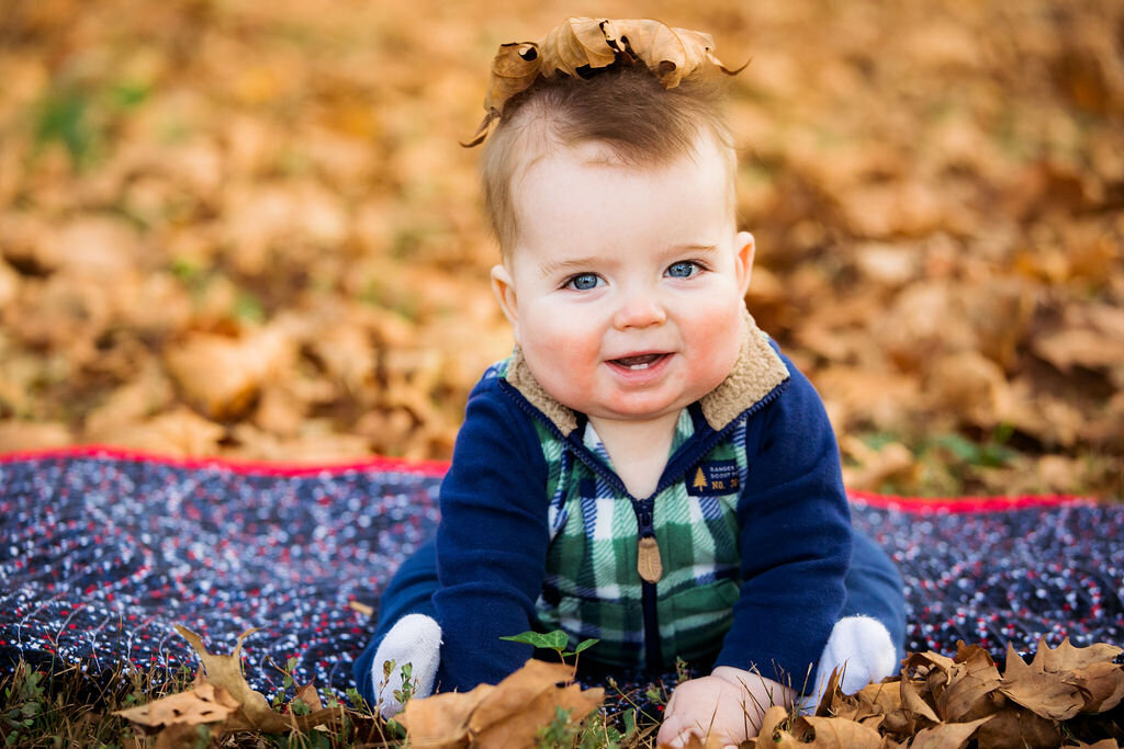 A kid sits outdoors in fall.