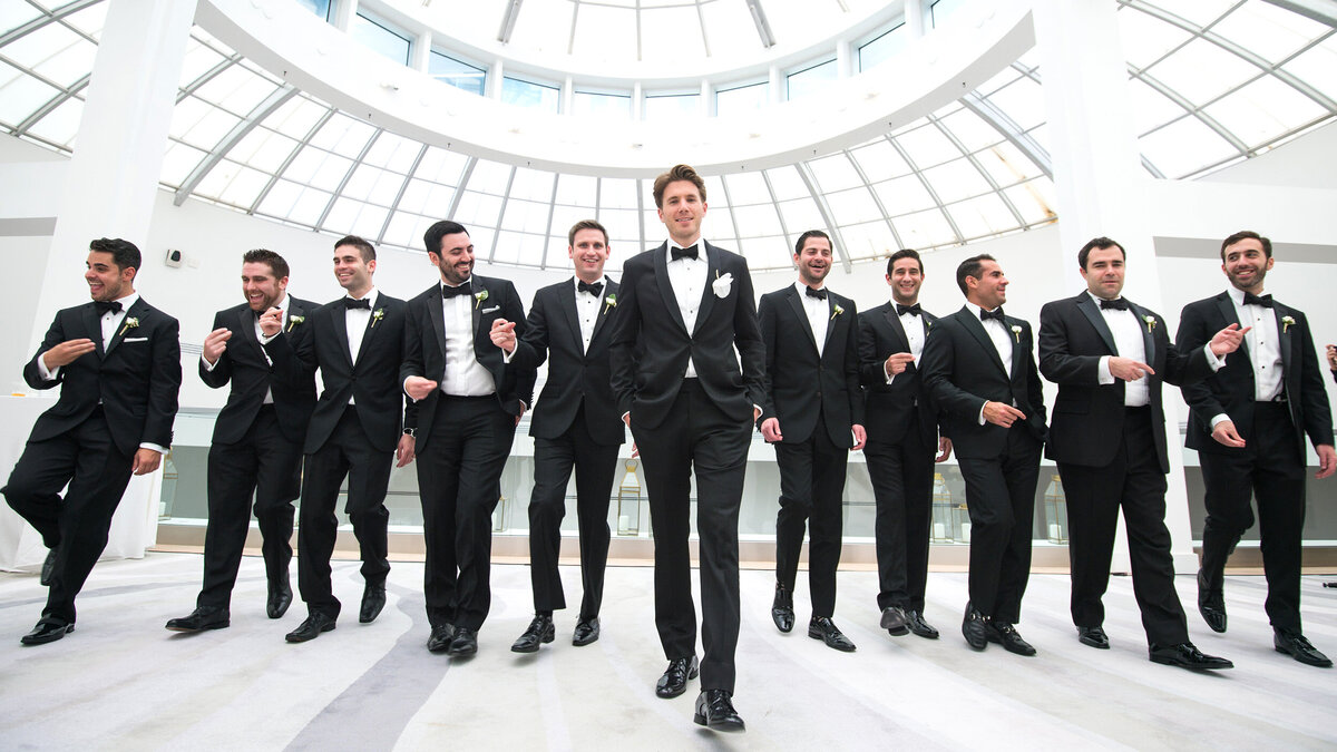 Joyful groomsmen in black tuxedos celebrating together, captured by Rodrigo Varela Photography.