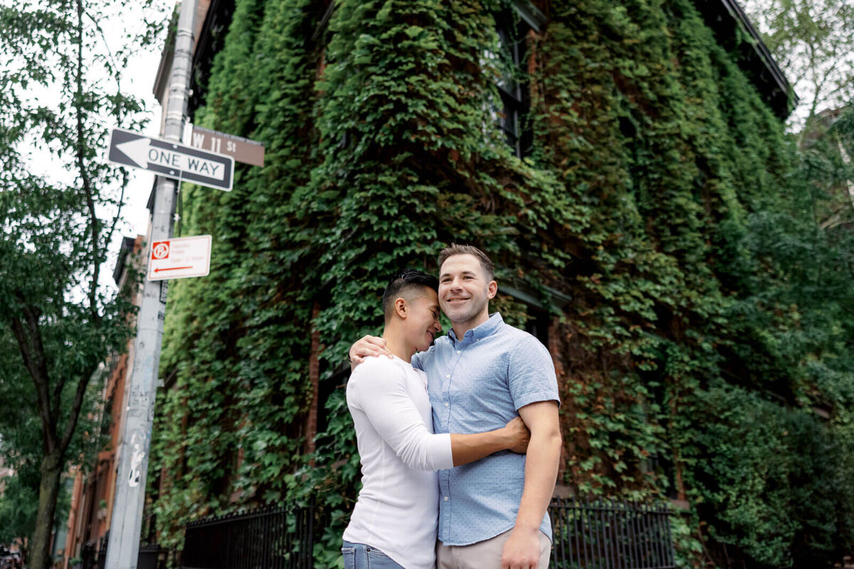The engaged man is hugging his fiancé in front of an ivy-covered building in West Village, NYC. Image by Jenny Fu Studio