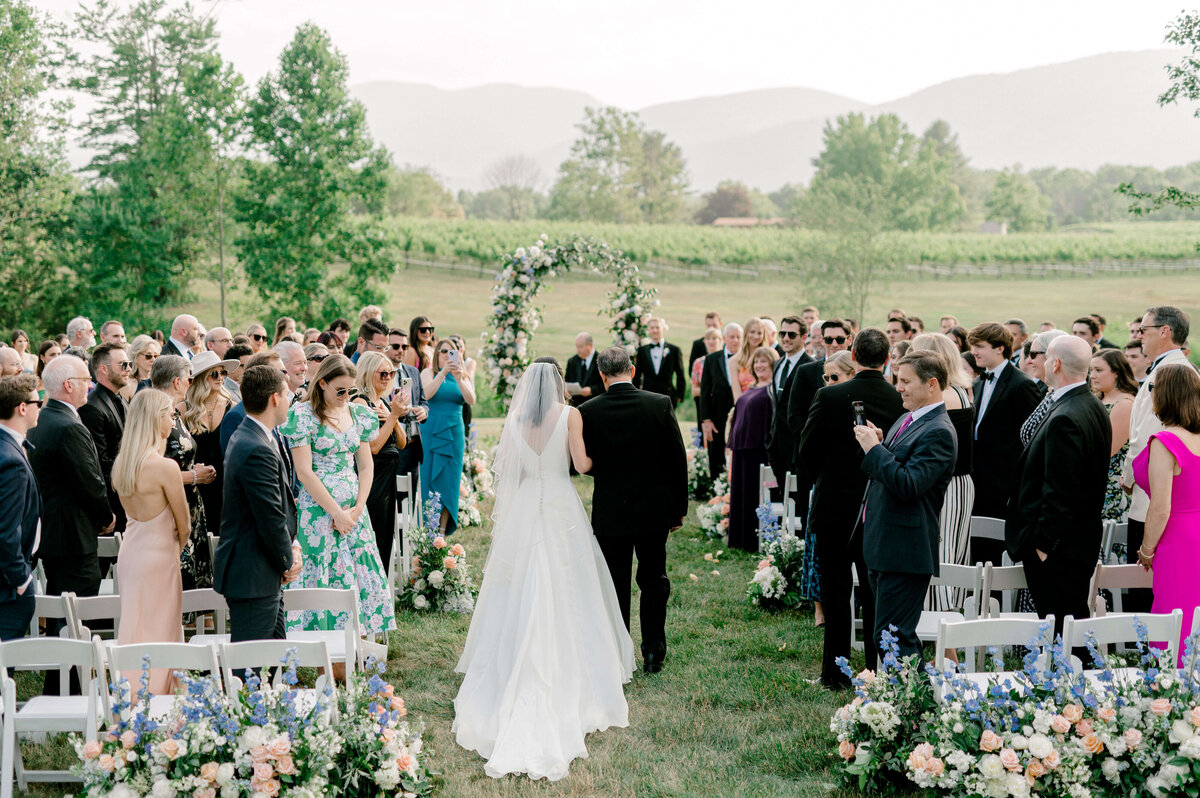 Wide shot of a bride walking down a floral lined aisle to her groom during her Northern Virginia wedding.