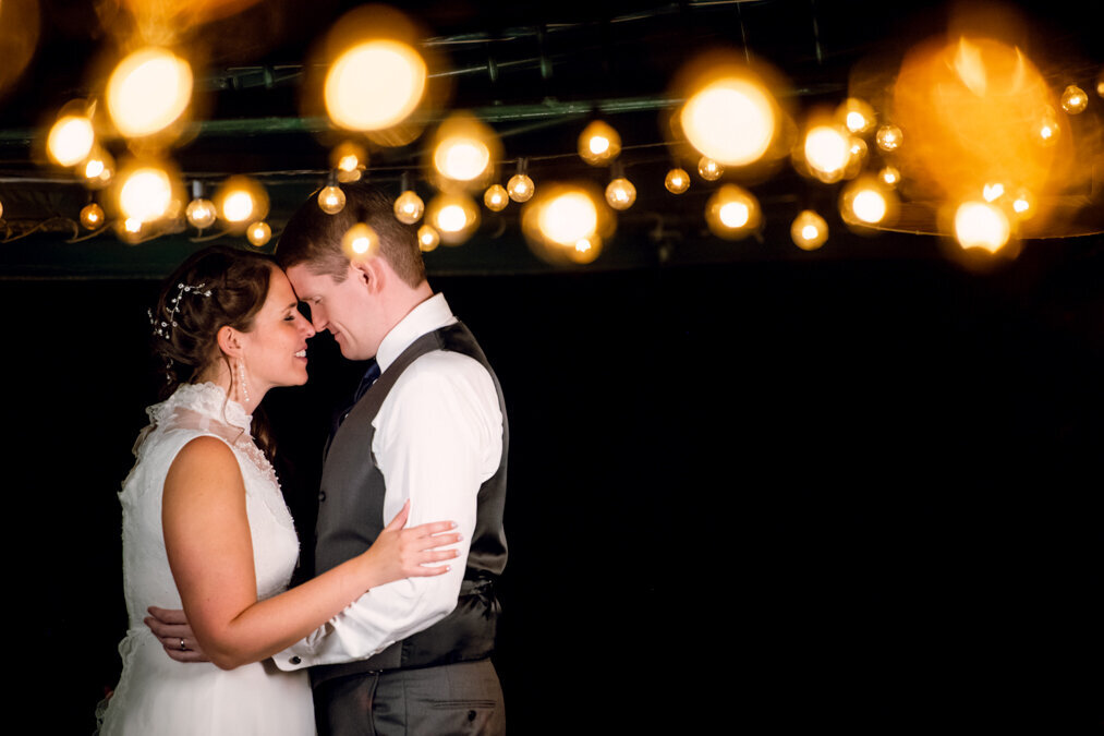 A bride and groom embracing under string lights.