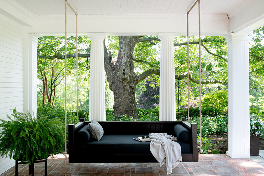 Interior design Boston features a black hanging daybed on a covered porch, blending modern exterior spaces with the charm of a historic home.