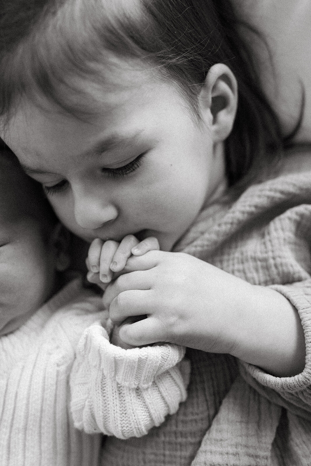 Close-up of toddler girl kissing her newborn baby brother’s hand during a documentary newborn photo session