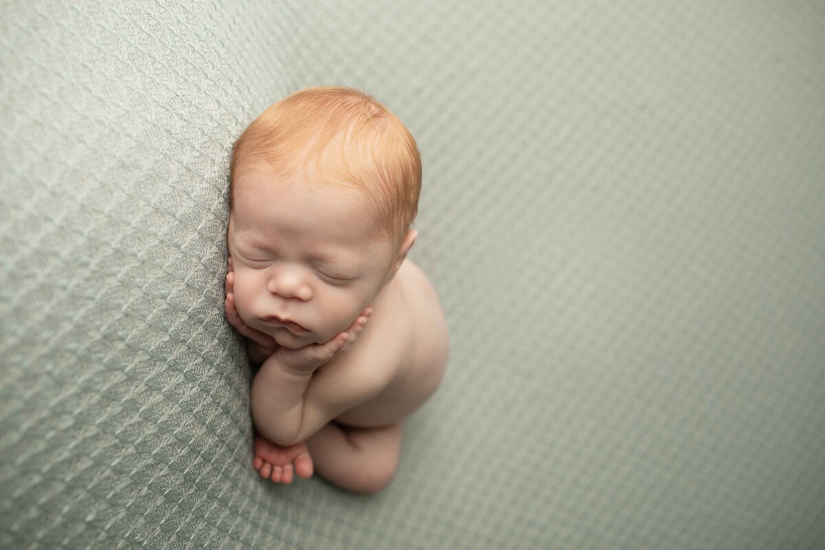Curled-up redhead newborn baby boy, wrapped in a cozy swaddle, eyes closed