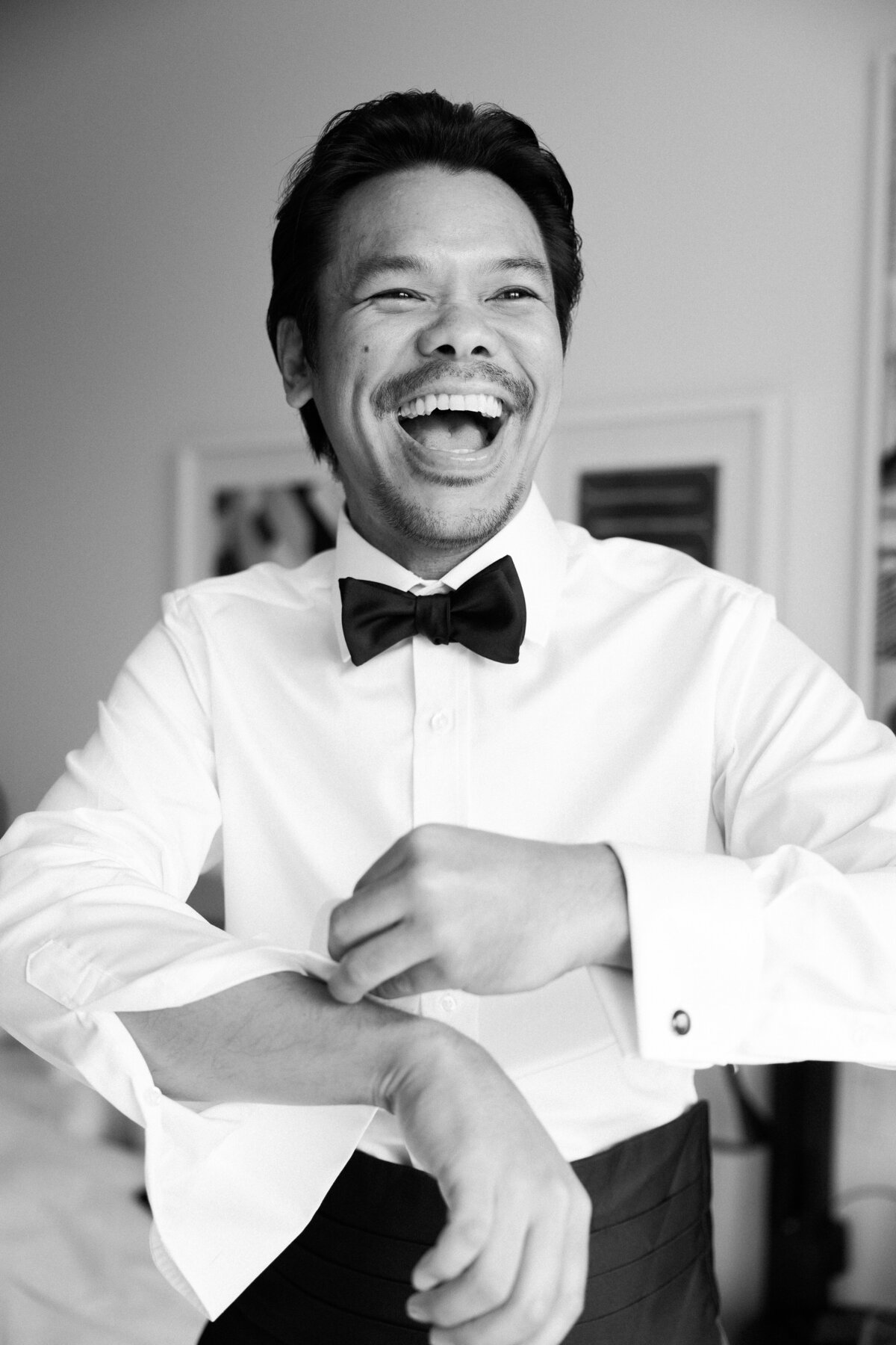 Groom laughs while buttoning his shirt 