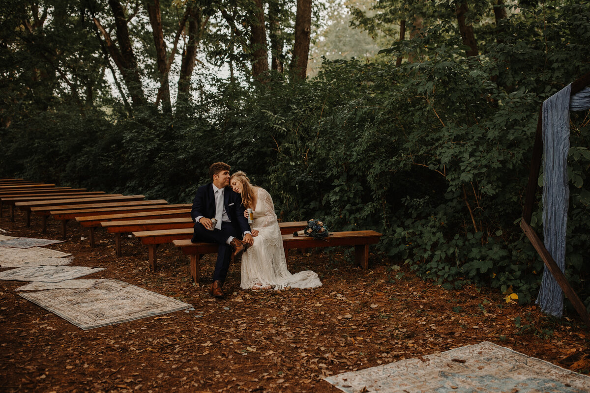 Couple sit cuddled up alone on seating at wedding ceremony site at Camp Wokanda in Peoria, IL while having some fresh bevs.