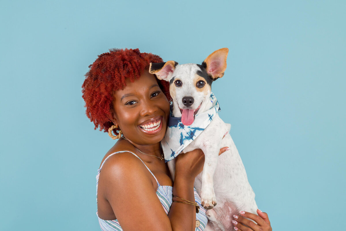 Woman with red afro holding jack Russell terrier on blue backdrop