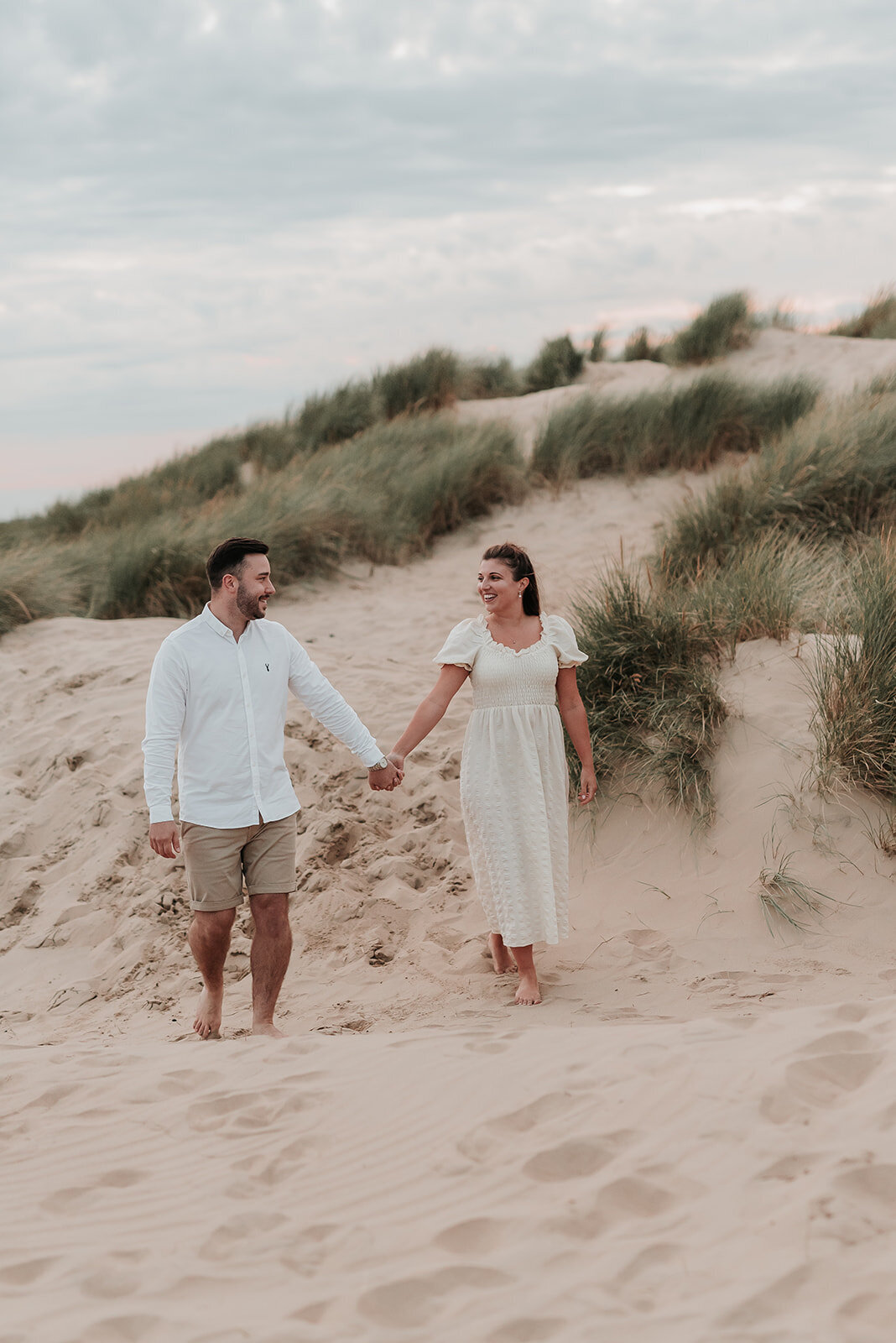 Couple hold hands as they walk bare foot in the sand at Camber Sands, Rye