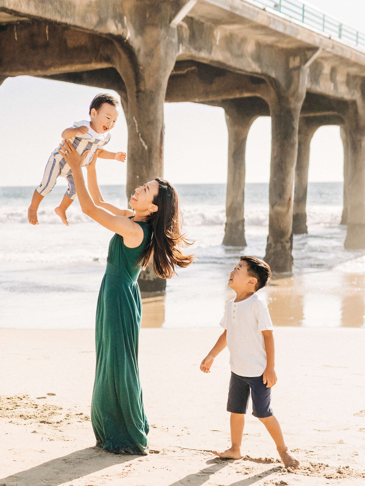 Mom is wearing a green dress. Mom holding baby up in the air.