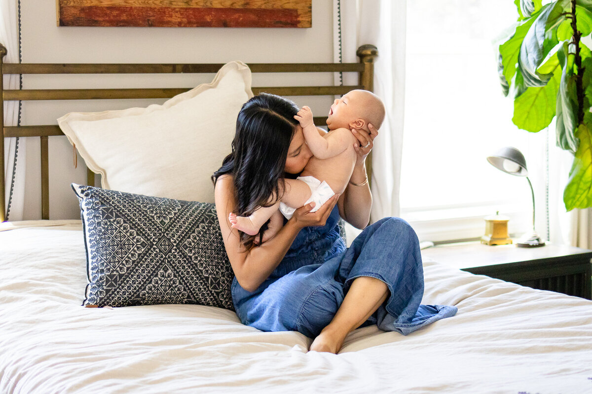 Candid moment of mother kissing baby’s stomach on bed, taken by San Francisco newborn photographer.
