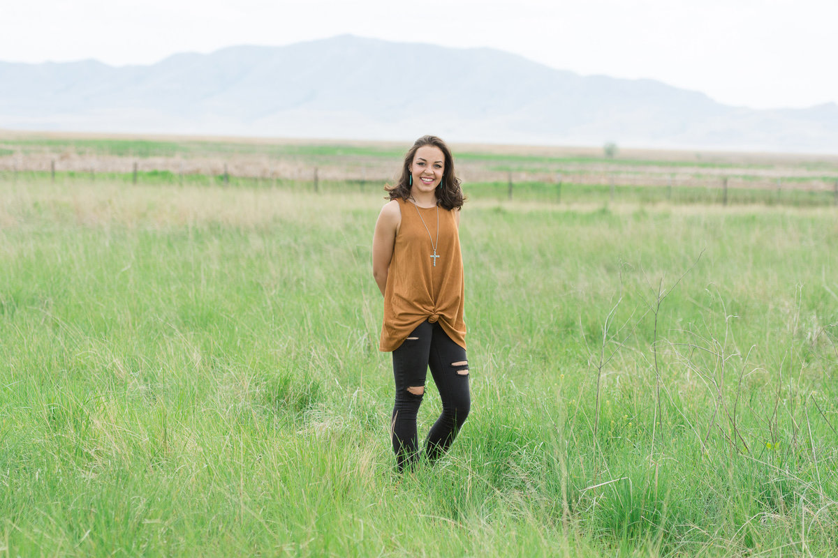 senior girl stands in grassy field during senior session in syracuse utah