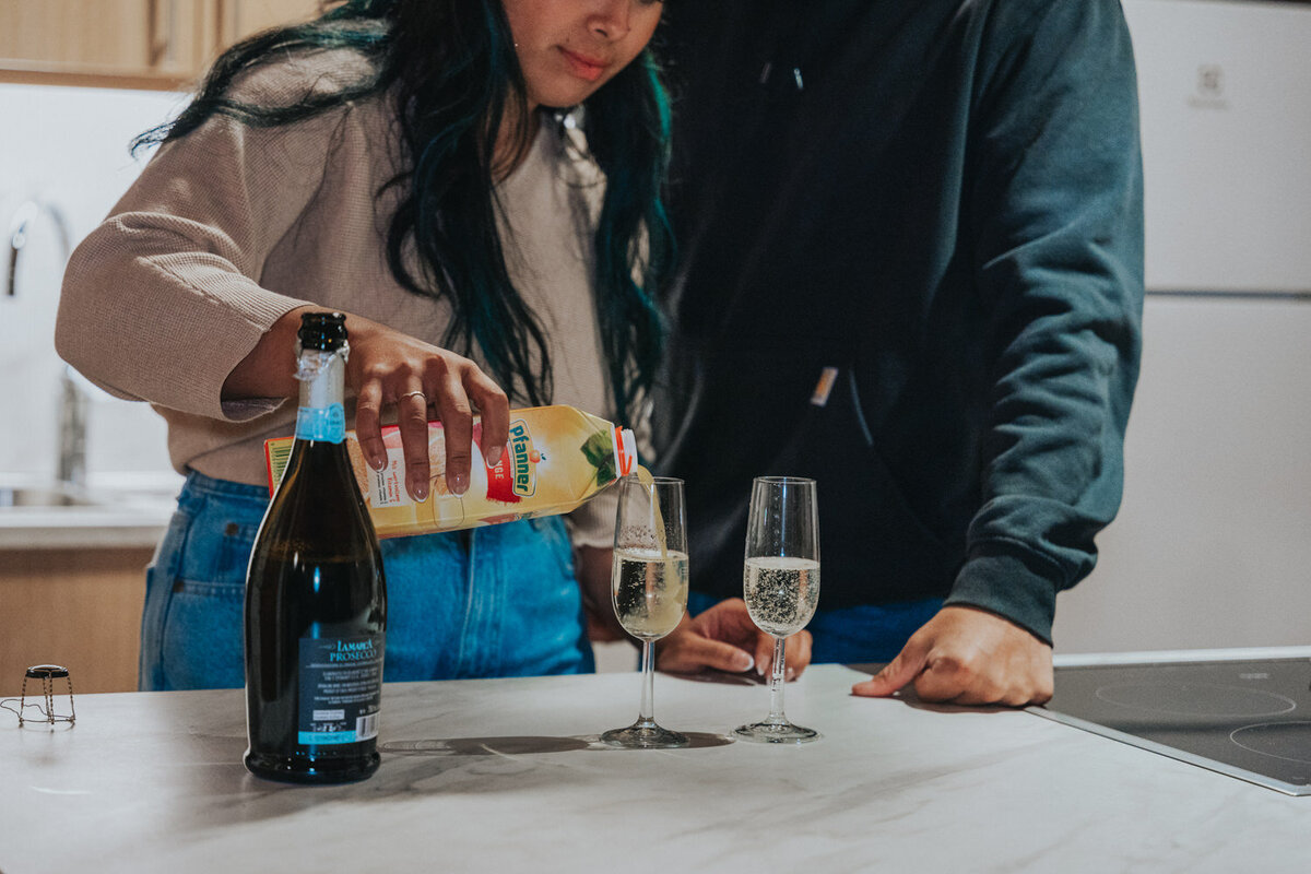 Wife pours orange juice into champagne glasses for mimosas 