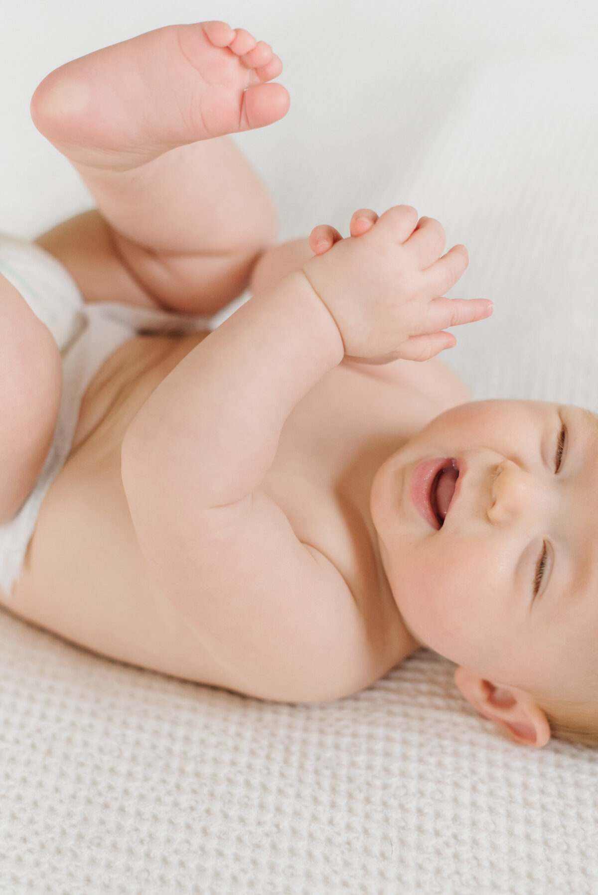 Baby laughing and laying on white blanket