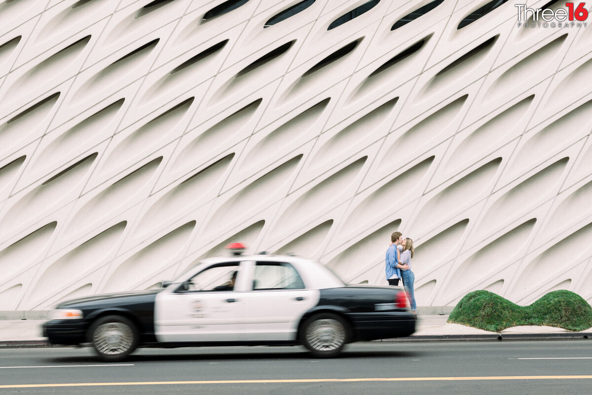 Engaged couple share a kiss at The Broad as a police car drives by