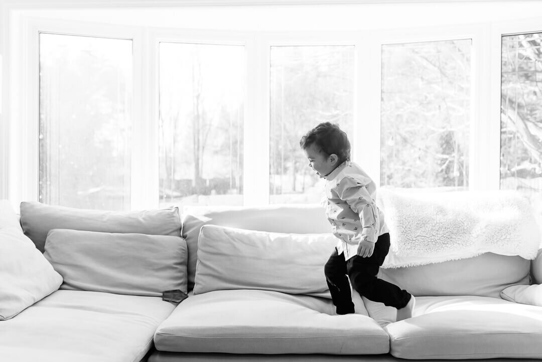 A black & white image of a young toddler running across a large sofa