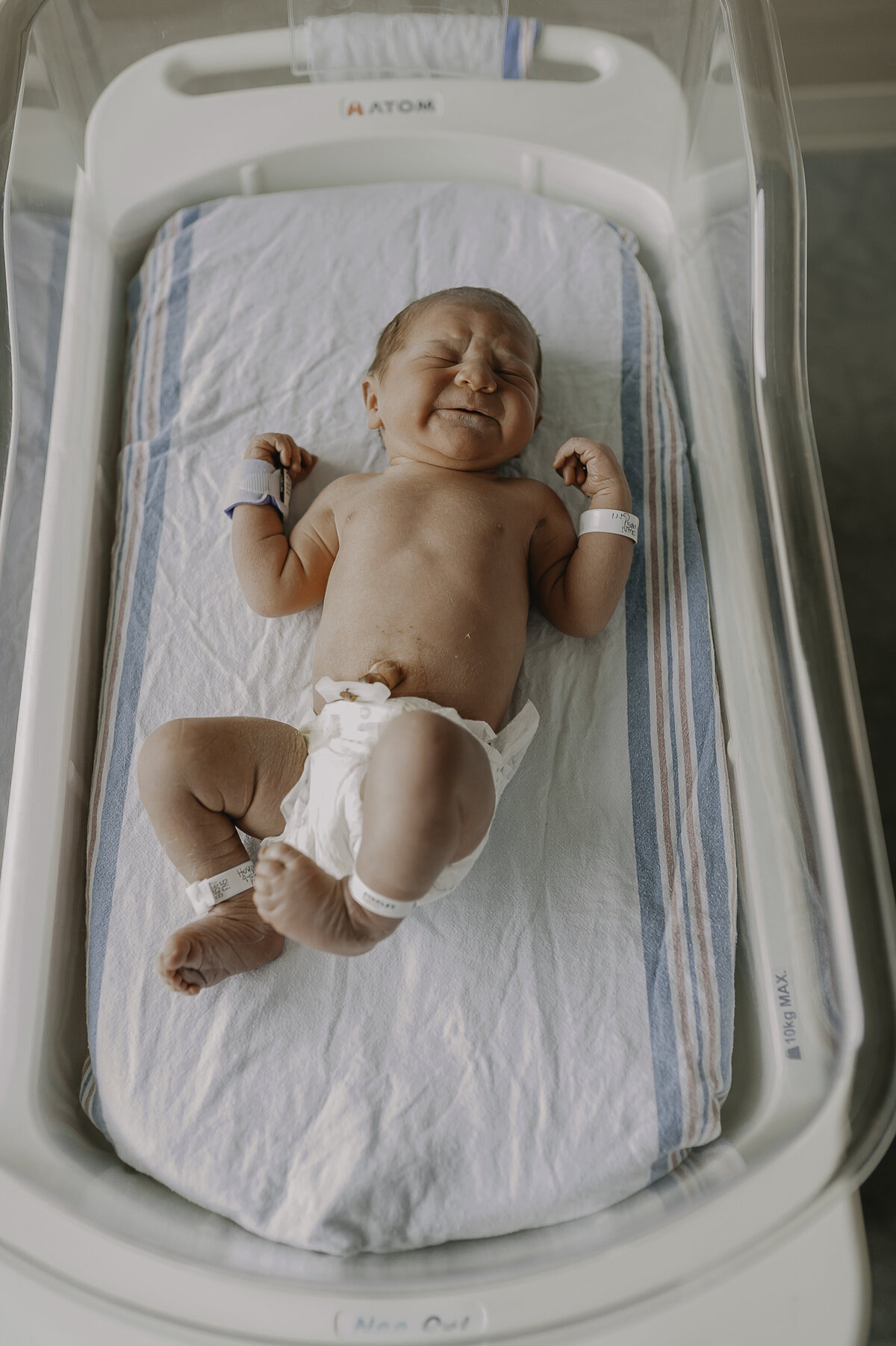 Verona B Photography captures a newborn baby in her diaper laying on the traditional hospital blanket in the hospital bassinet as cries after being separated from mommy’s warm arms. There is something awe-inspiring about these Fresh 48 sessions as they capture the newness of bringing another little life into the world – Akron General Hospital session.