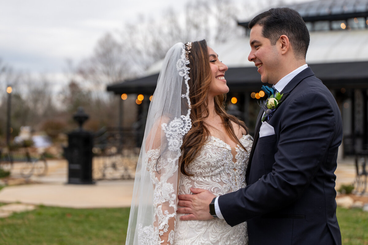 A wedding couple with their arms around each other smiling at each other 