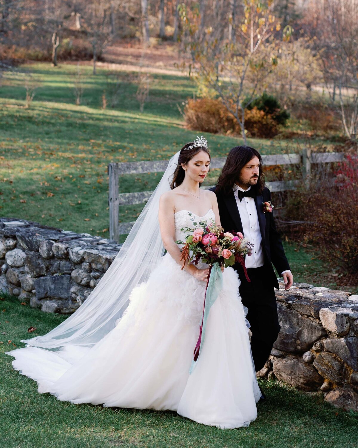 marchesa bride walks across green lawn with jennifer behr crown and stone walls