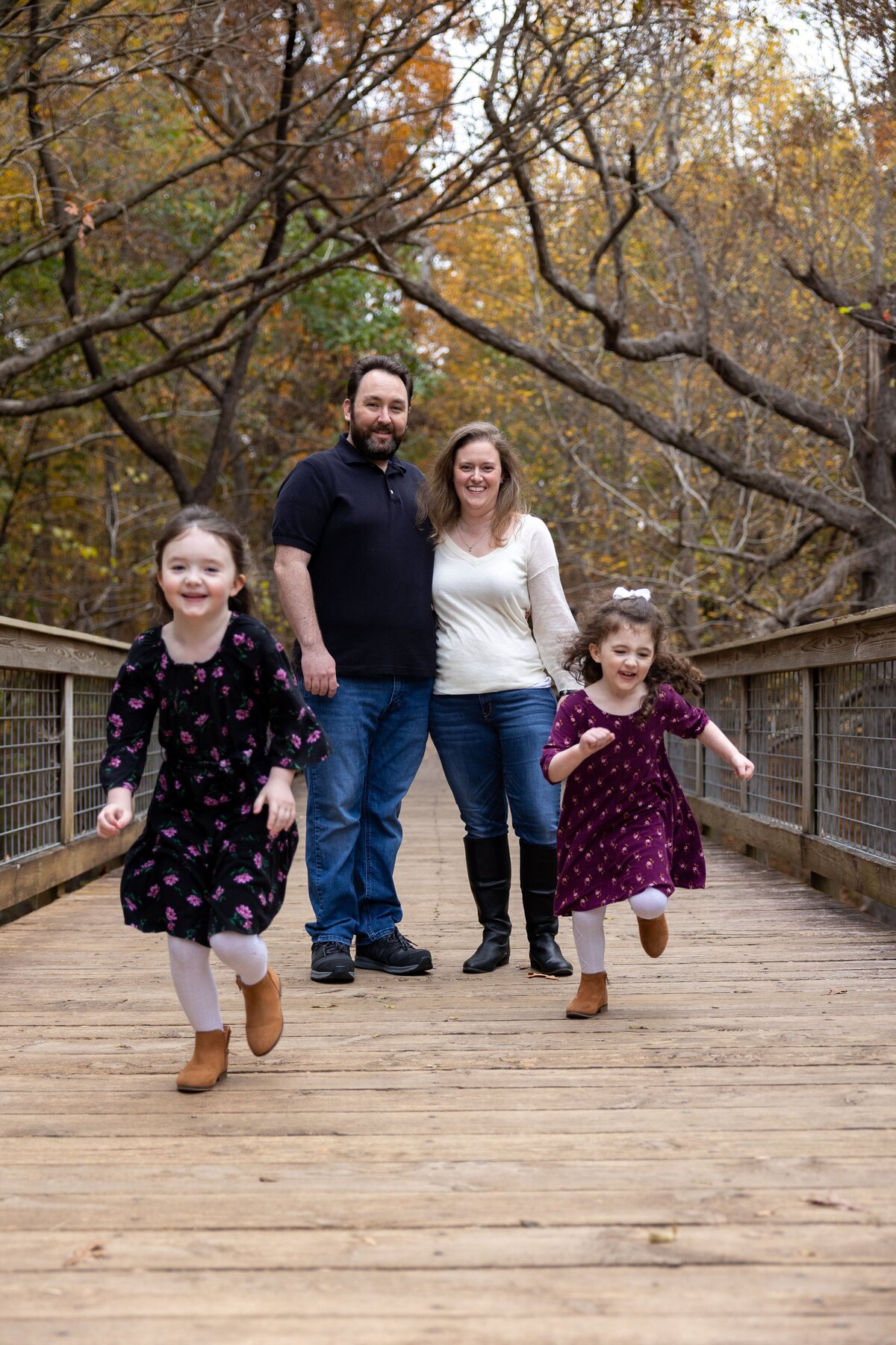 a mom and dad standing on a bridge with two children running