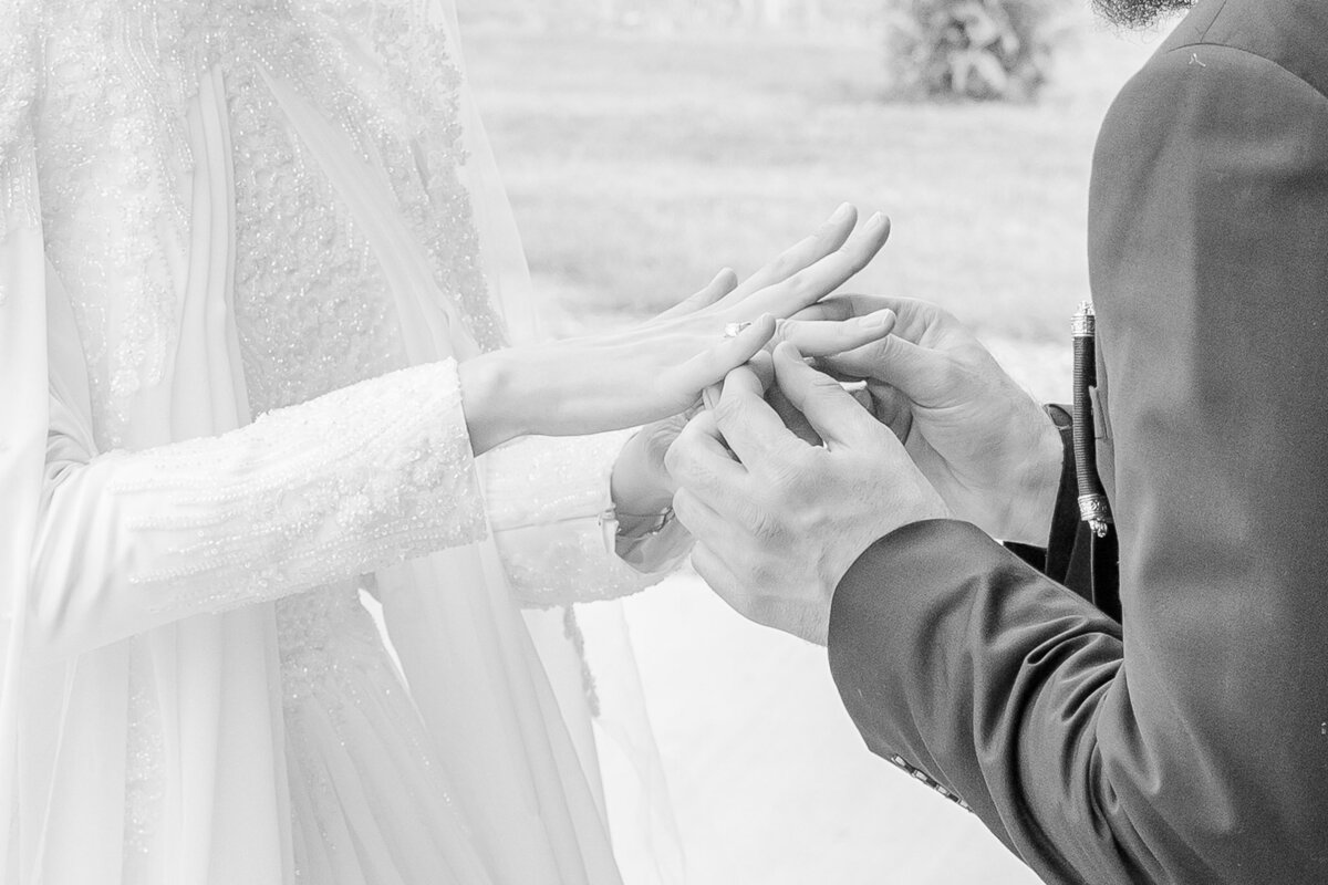 An action shot of a groom putting on his bride's wedding ring mid wedding ceremony.